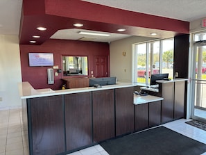 A reception desk with a computer, a mirror, and a window with a view of parked cars outside. - Red Roof Inn Wildwood, FL - The Villages (Wildwood)
