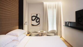 Ein modernes Hotelzimmer mit einem großen Bett, zwei Sesseln, einem kleinen Tisch, einem an der Wand montierten Fernseher und einem großen abstrakten Gemälde.
