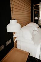 A modern hotel room with a wooden headboard, a white bed, and a bedside table.