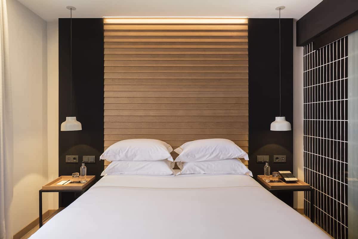 A modern hotel room with a large bed, two bedside tables, and a wooden headboard.