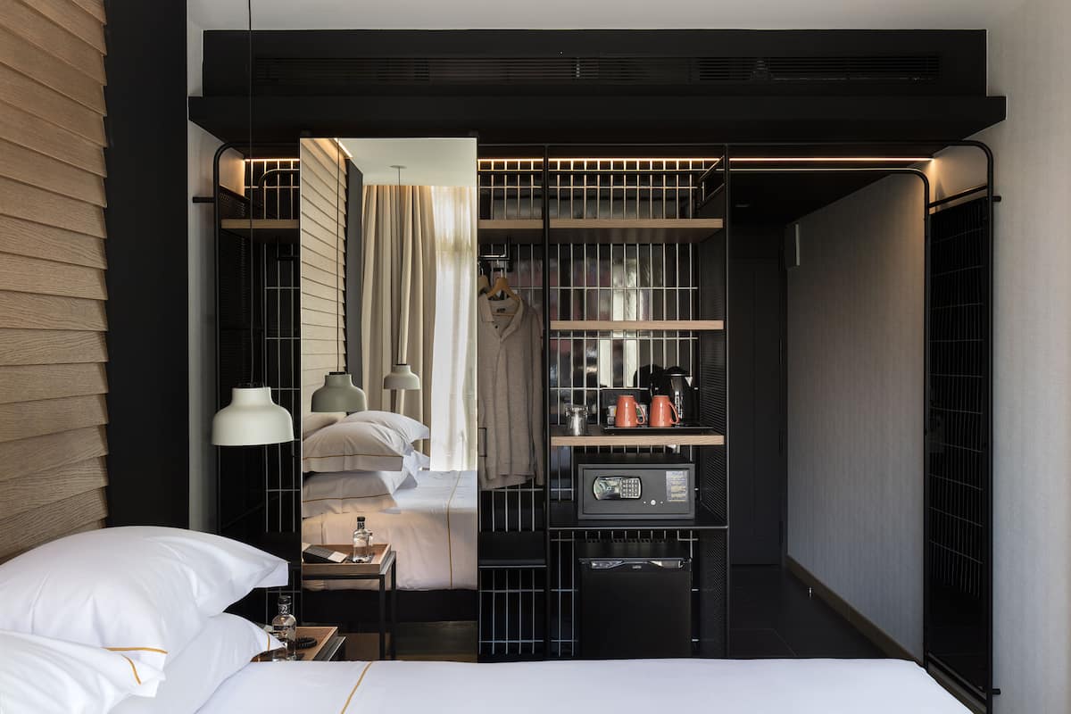 A modern hotel room with a bed, bedside table, lamp, and a built-in wardrobe with a mirror and shelves.