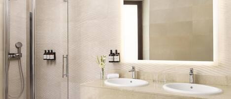 Un baño moderno con ducha de vidrio, dos lavamanos y un espejo grande.