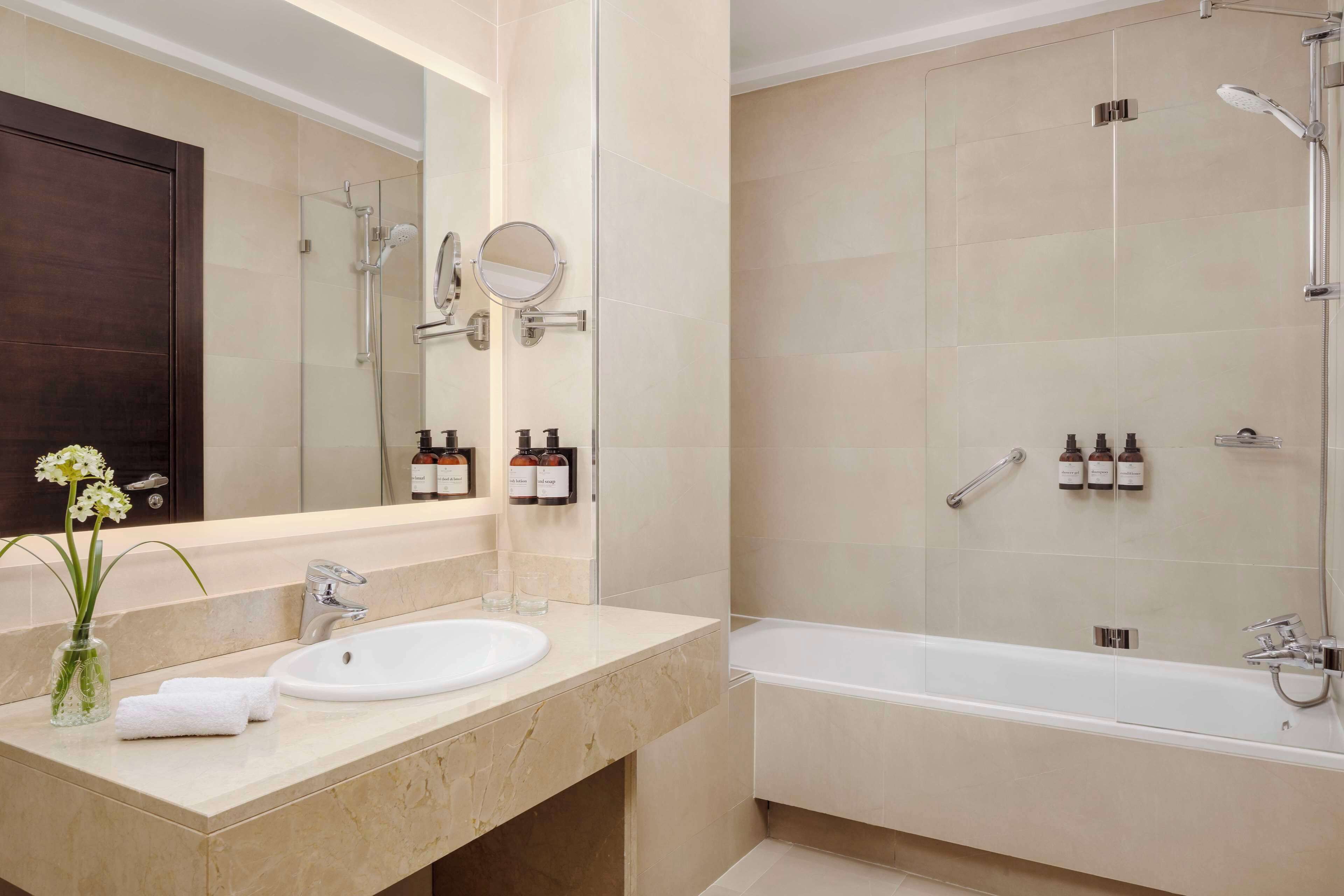 Un baño moderno con un espejo grande, un lavamanos, una bañera y un box de ducha.