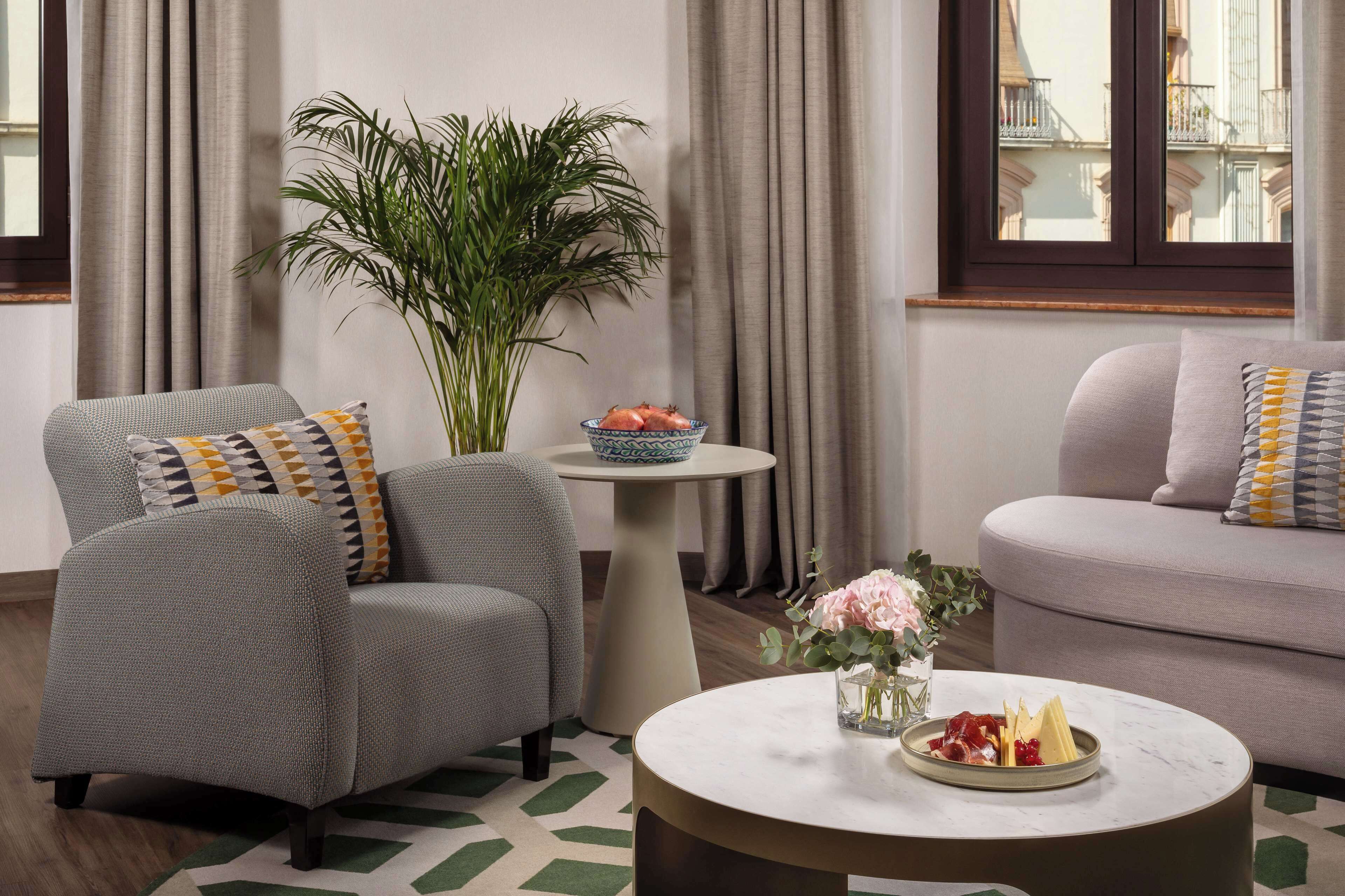 Un salon moderne avec un canapé gris, une table basse ronde agrémentée d’un arrangement floral et une plante en pot.