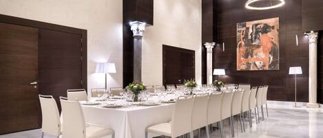 Una larga mesa de comedor dispuesta para una comida formal, rodeada de sillas, con una lámpara moderna y obras de arte en las paredes.