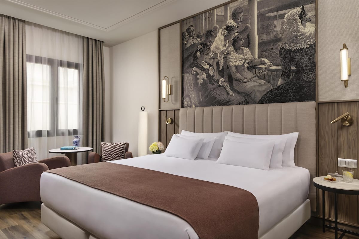 A hotel room with a large bed, a seating area with a table, and a wall-mounted artwork.