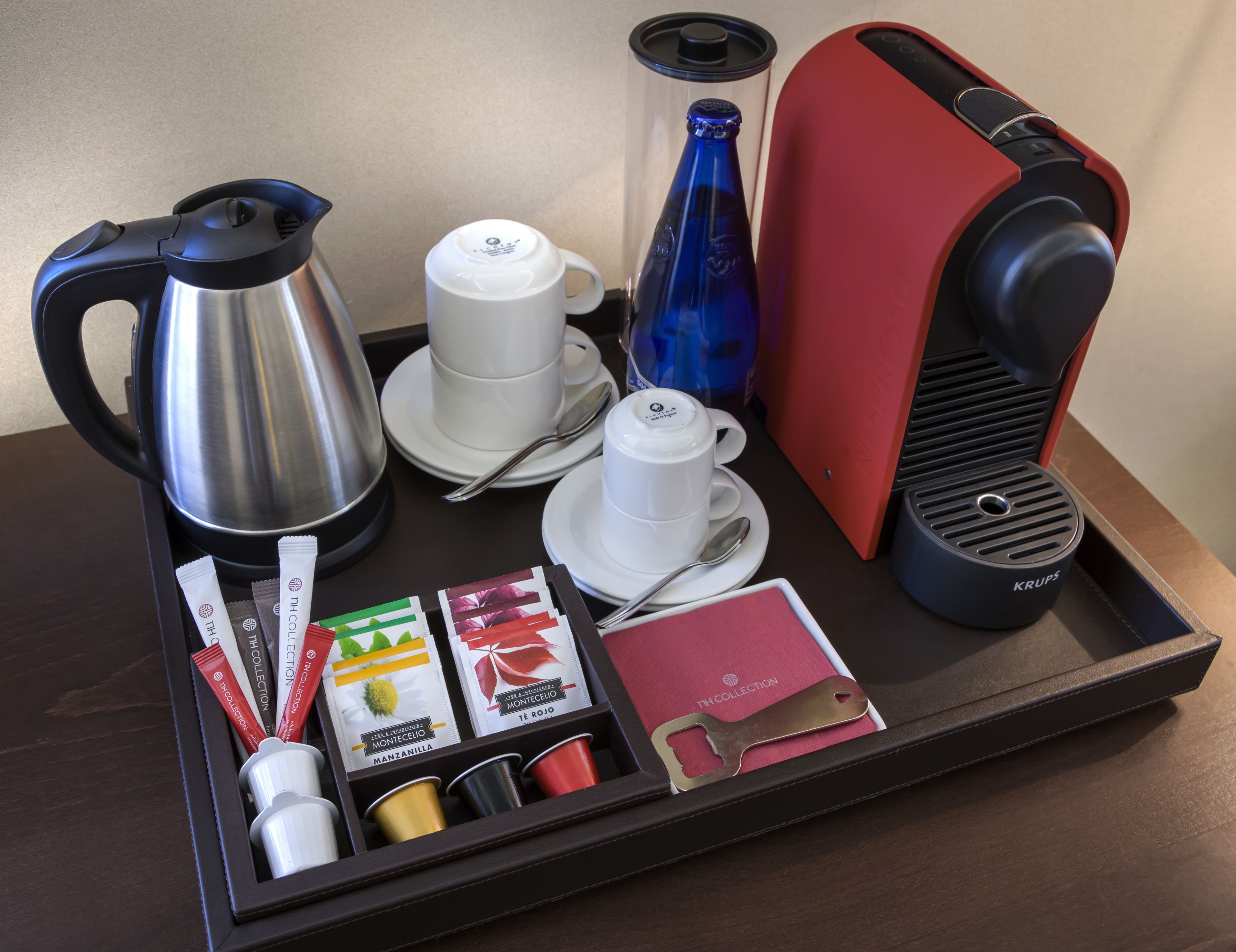 Uma bandeja com cafeteira, chaleira, uma garrafa azul, uma máquina de café vermelha e sachês de chá.