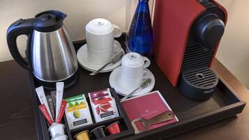 Uma bandeja com cafeteira, chaleira, uma garrafa azul, uma máquina de café vermelha e sachês de chá.
