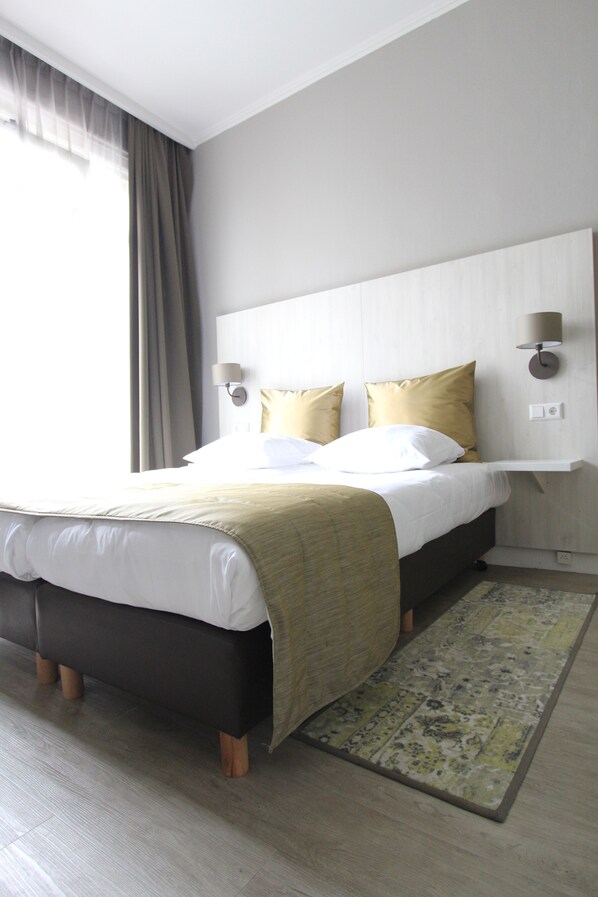A hotel room with a bed, a bedside table, a lamp, and a window with curtains.