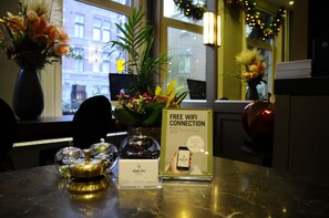 A hotel reception area with a 'Free WiFi Connection' sign, a vase with flowers, and a decorative item on the counter.