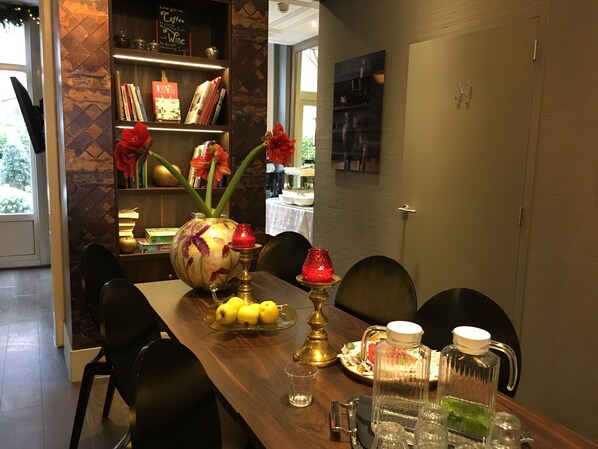 A dining table with a vase of flowers, a candle, and a bottle of water. There are chairs around the table and a bookshelf in the background.