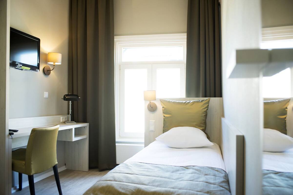 Hotellihuone, jossa on sänky, työpöytä, tuoli, televisio ja ikkuna, jossa on verhot.