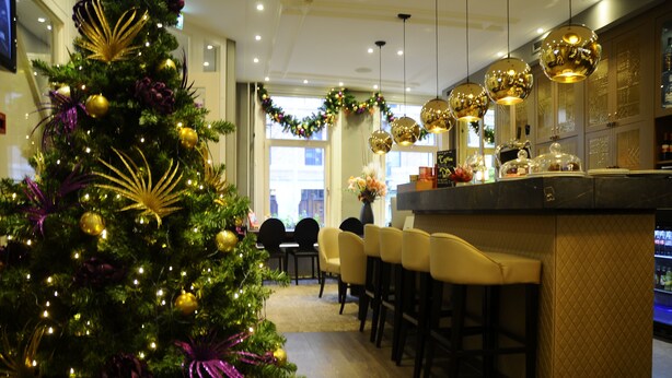 A modern hotel lobby with a Christmas tree, bar area, and seating. - Apple Inn Hotel (Amsterdam)