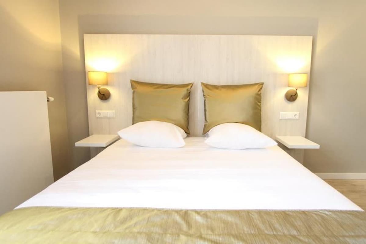 A bed with two pillows, a bedside table, and wall-mounted lamps.