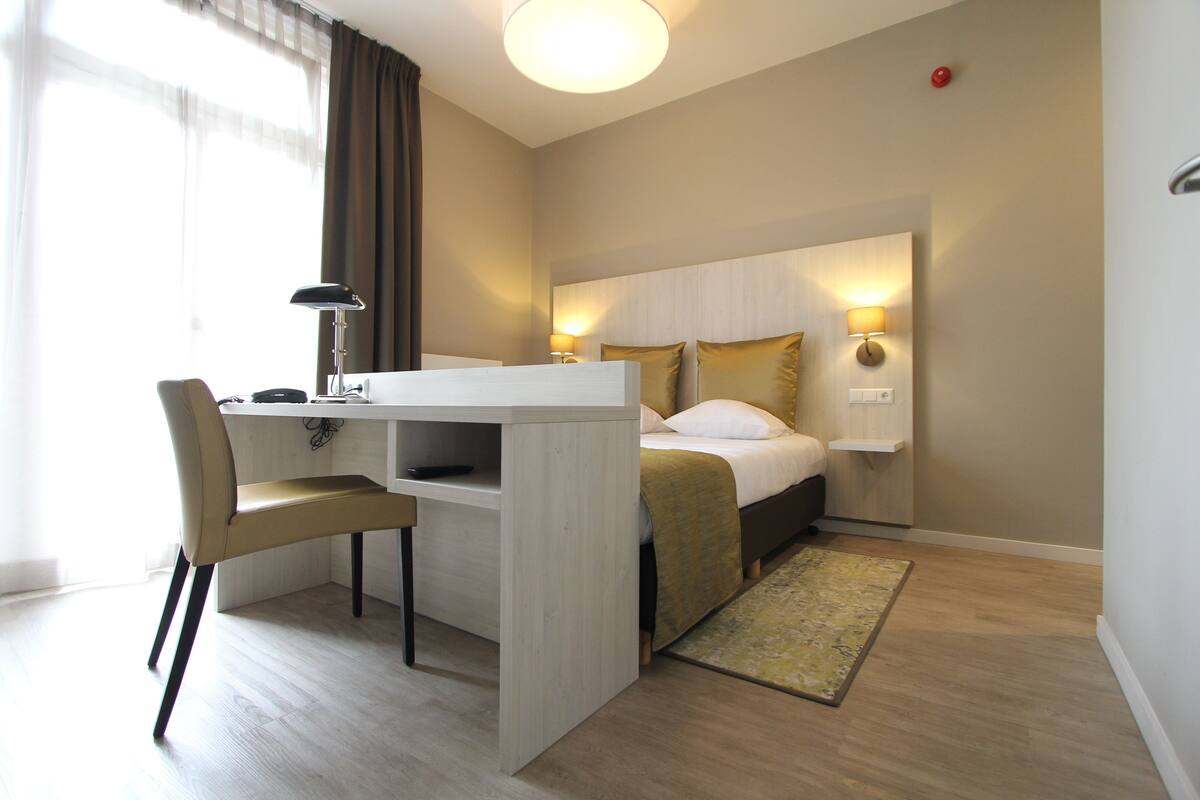 Hotellihuone, jossa on sänky, yöpöydät, työpöytä tuolilla ja pieni matto.