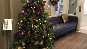 A Christmas tree with gold and purple ornaments, a grey sofa, and a television mounted on the wall. - Apple Inn Hotel (Amsterdam)