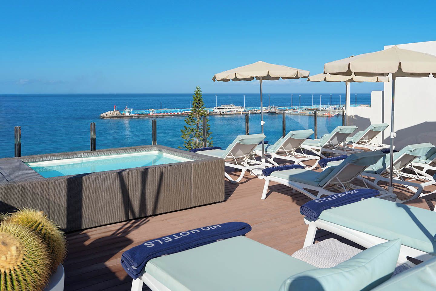 A rooftop pool area with lounge chairs and umbrellas, overlooking a body of water.