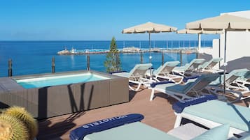 A rooftop pool area with lounge chairs and umbrellas, overlooking a body of water.