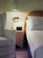 A hotel room with a bed, a nightstand with a lamp, a clock, and a chair.