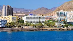 A coastal cityscape with a prominent hotel marked 'HOTEL H10' and a mountain backdrop. - H10 Big Sur Boutique Hotel (Arona)