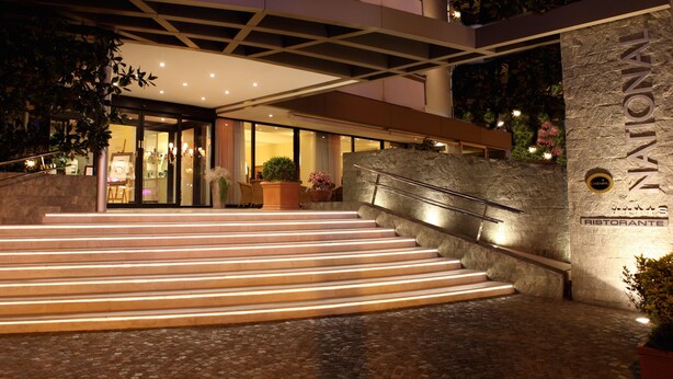 A hotel entrance with a stone facade, a staircase leading to the entrance, and a sign indicating a restaurant. - National Hotel (Rimini)