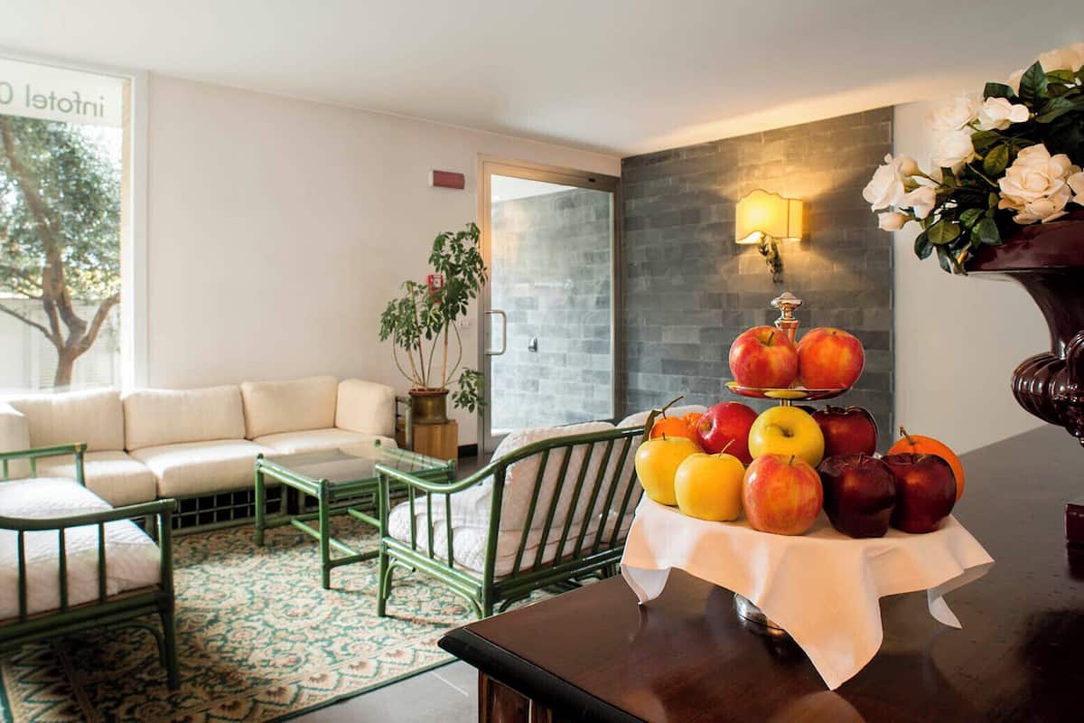 A cozy living room with a sofa, green chairs, a coffee table, and a fruit display on a table.