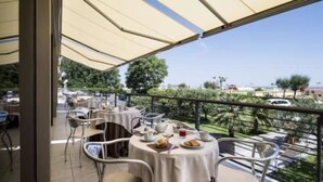 An outdoor dining area with tables and chairs, a view of the sea, and a clear sky. - National Hotel (Rimini)