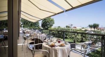 An outdoor dining area with tables and chairs, a view of the sea, and a clear sky.