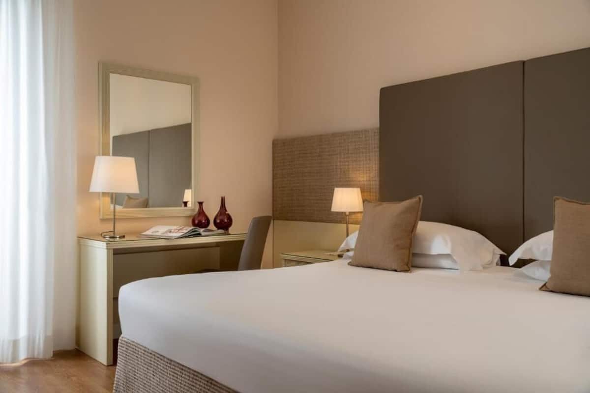 A hotel room with a large bed, bedside lamps, a nightstand, a mirror, and a headboard.