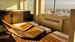A sunlit room with wooden loungers and a view of the city. - National Hotel (Rimini)
