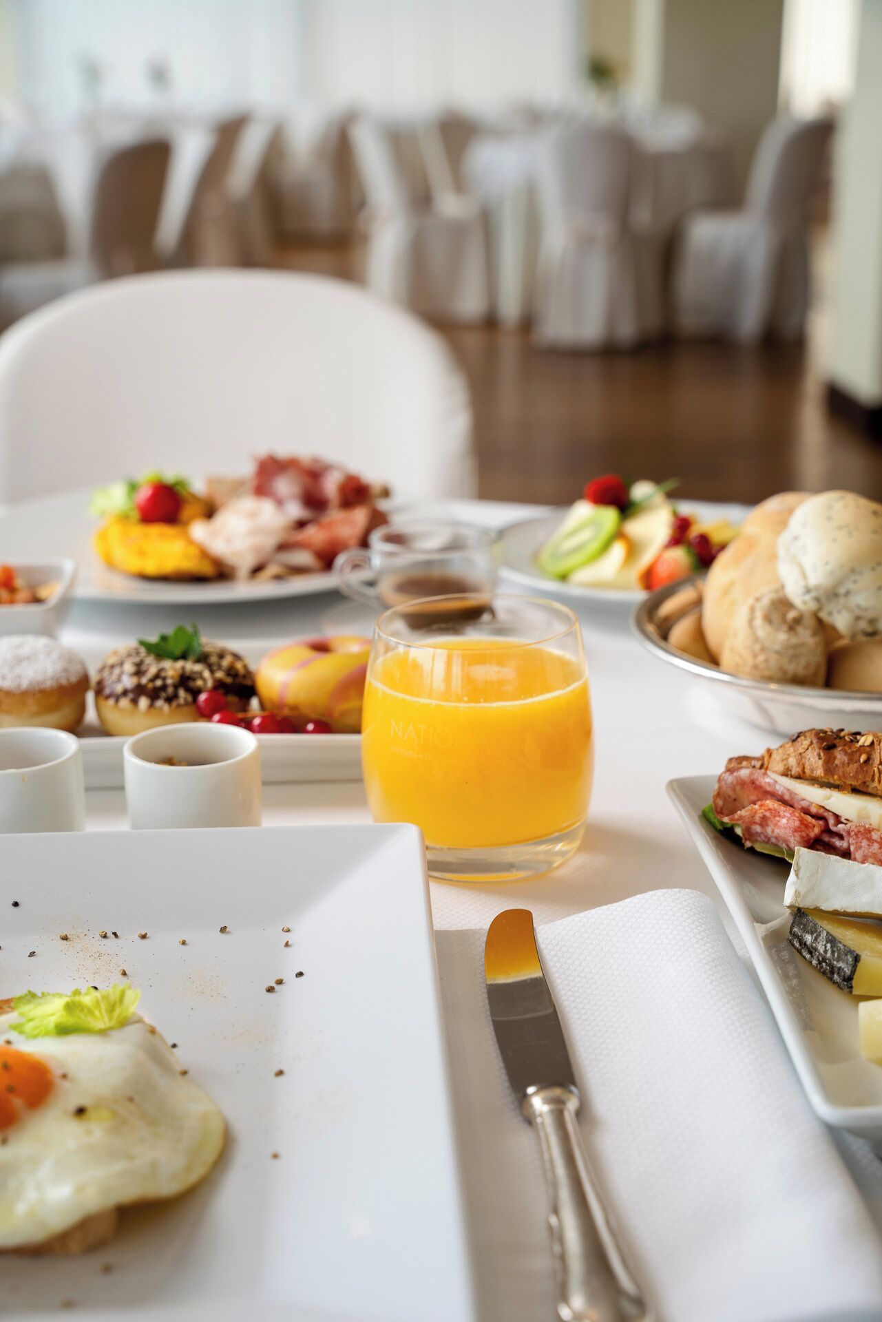 A breakfast buffet with various dishes, a glass of orange juice, and a knife and napkin on a white plate.