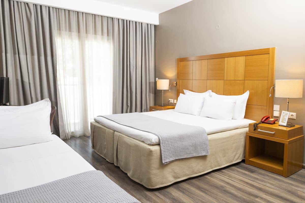 Habitación de hotel con una cama grande, una mesita de noche con lámpara, y un atril con teléfono y marco de fotos.