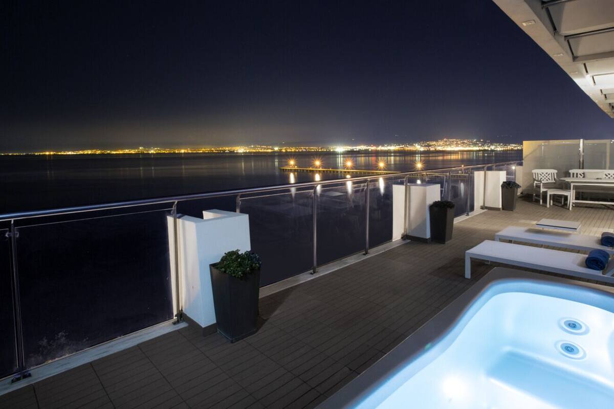Un balcón con hidromasaje, sillones de descanso y vistas a la ciudad de noche.