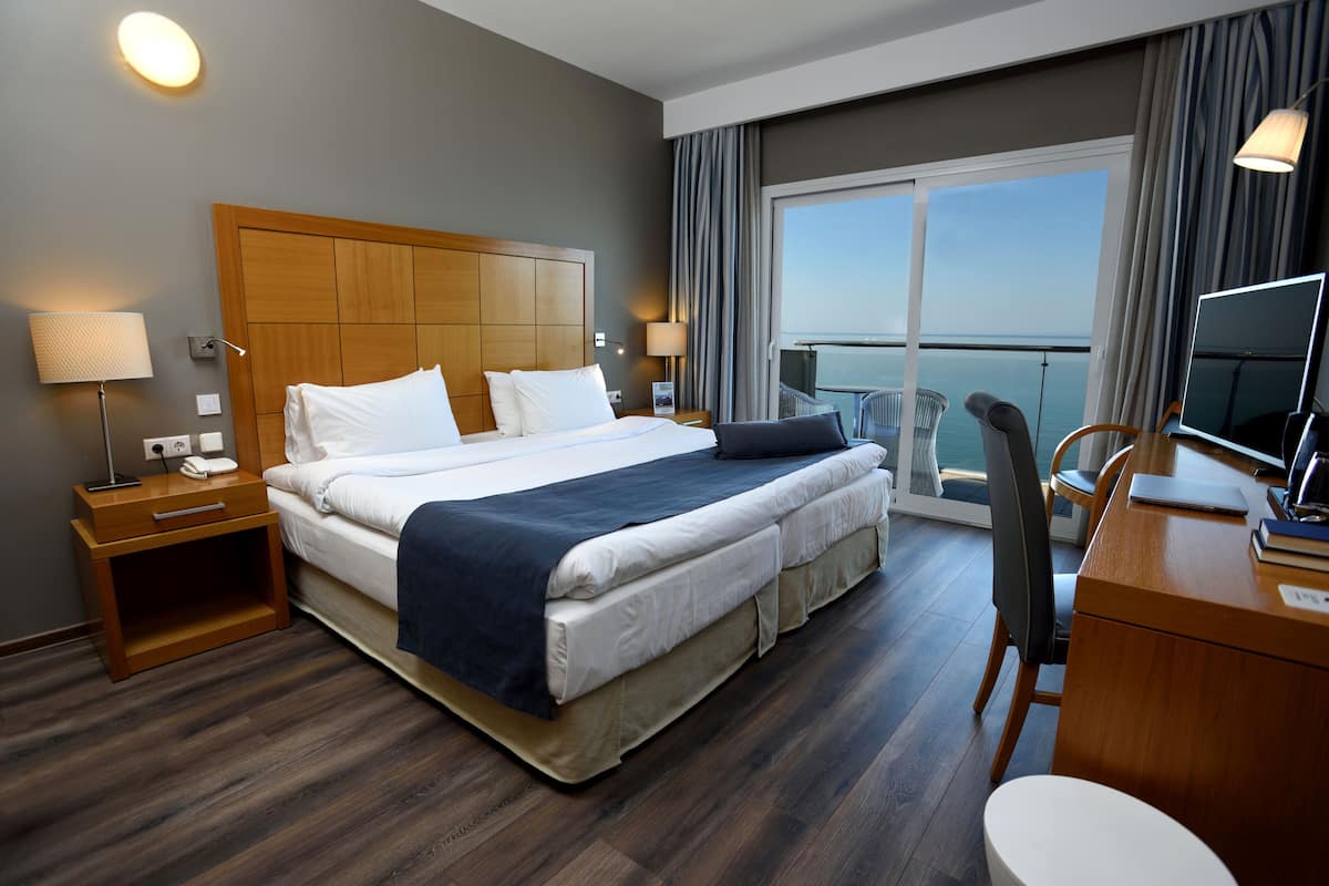 Habitación de hotel con una cama grande, un escritorio con una silla, un televisor y un balcón con vistas al mar.