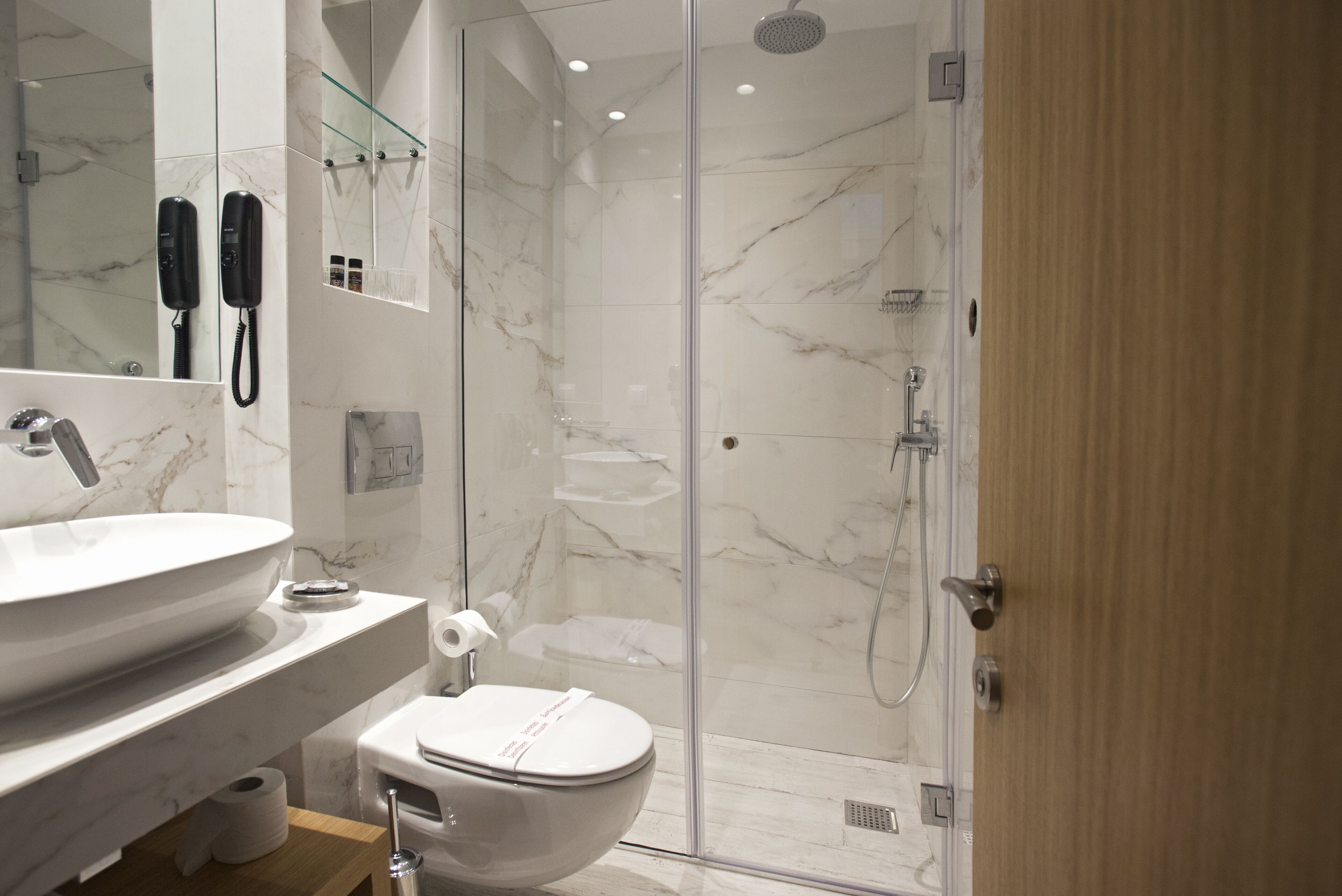 Un baño moderno con lavamanos, inodoro y ducha con mampara de vidrio de mármol.