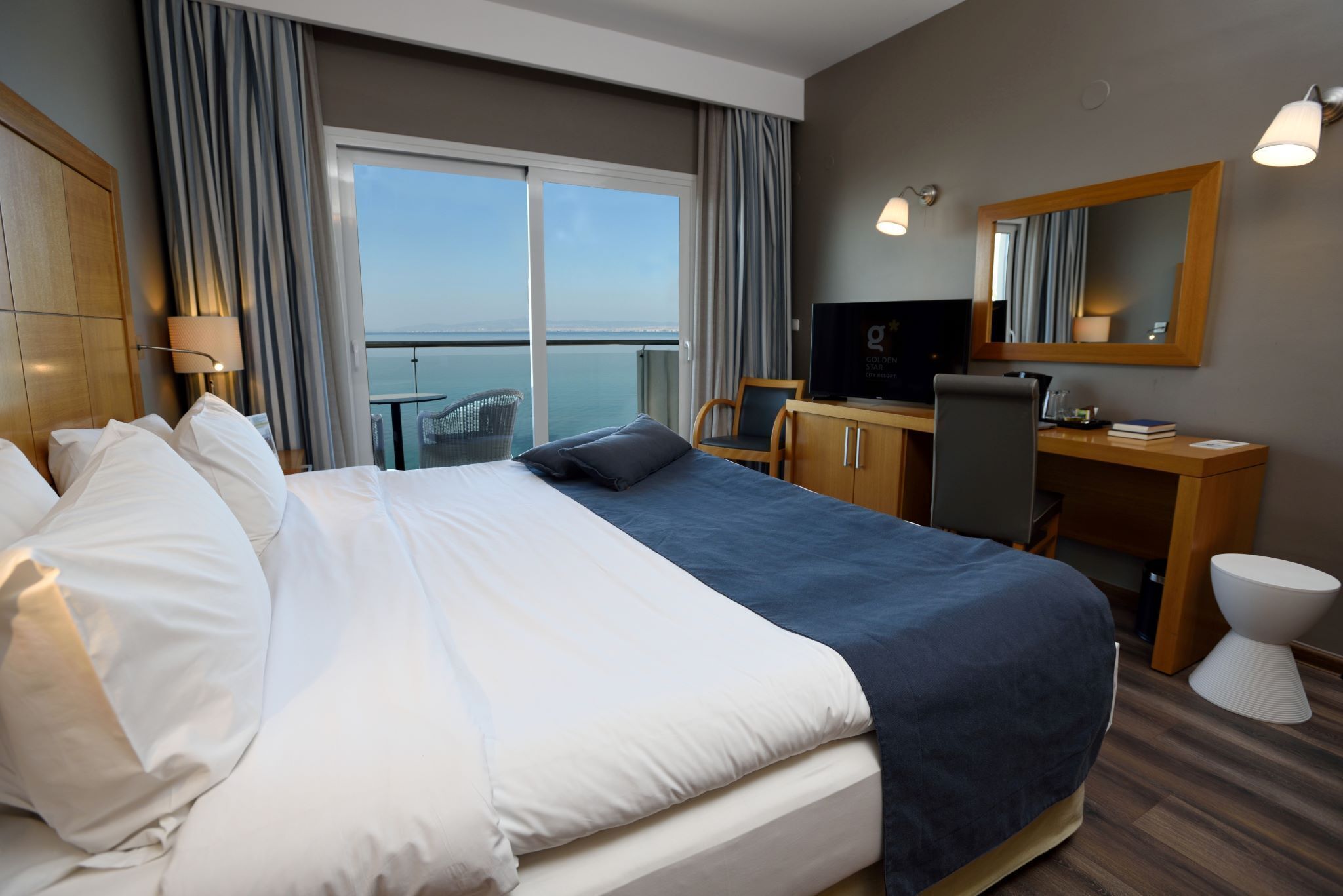 Habitación de hotel con una cama grande, un escritorio, un televisor y vista al mar.