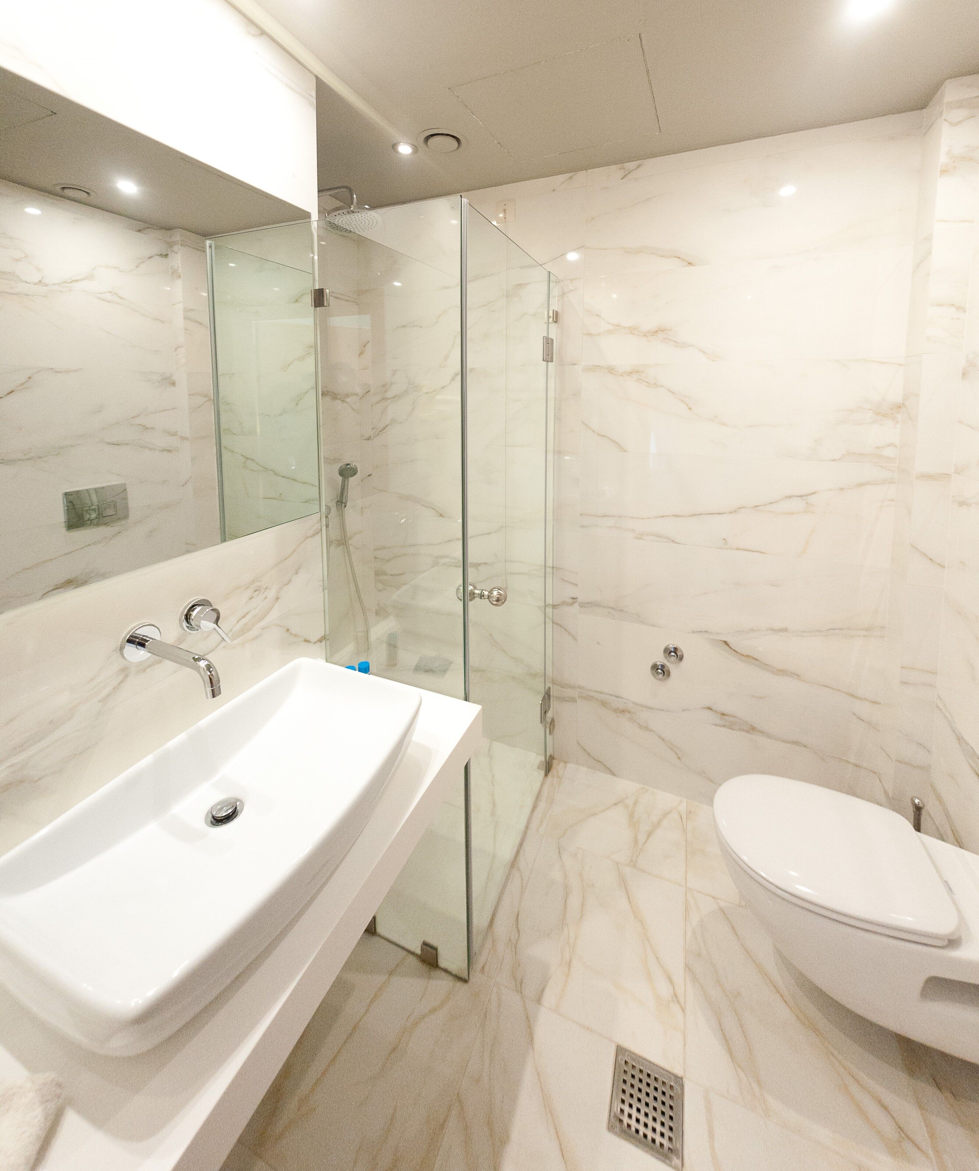 Une salle de bain moderne avec un lavabo en marbre, une douche en verre et des toilettes.