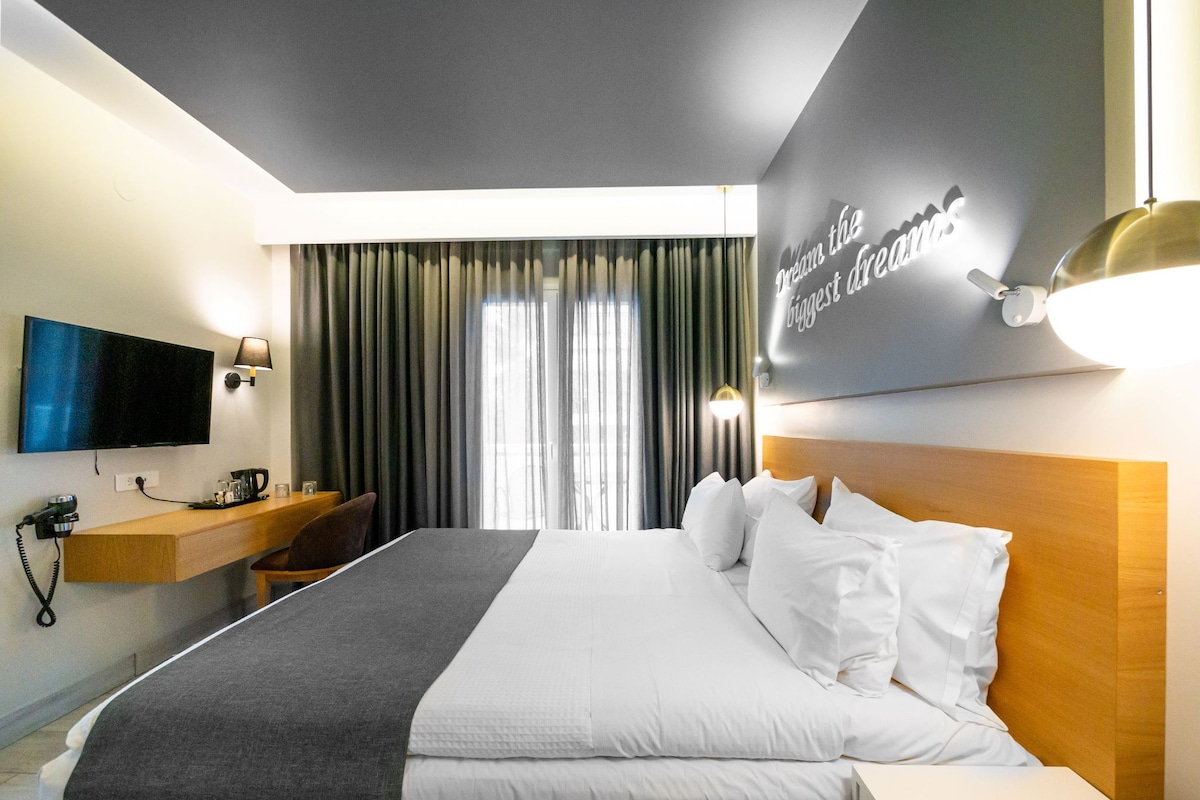 Habitación de hotel con cama, televisión, escritorio con lámpara y ventana con cortinas.