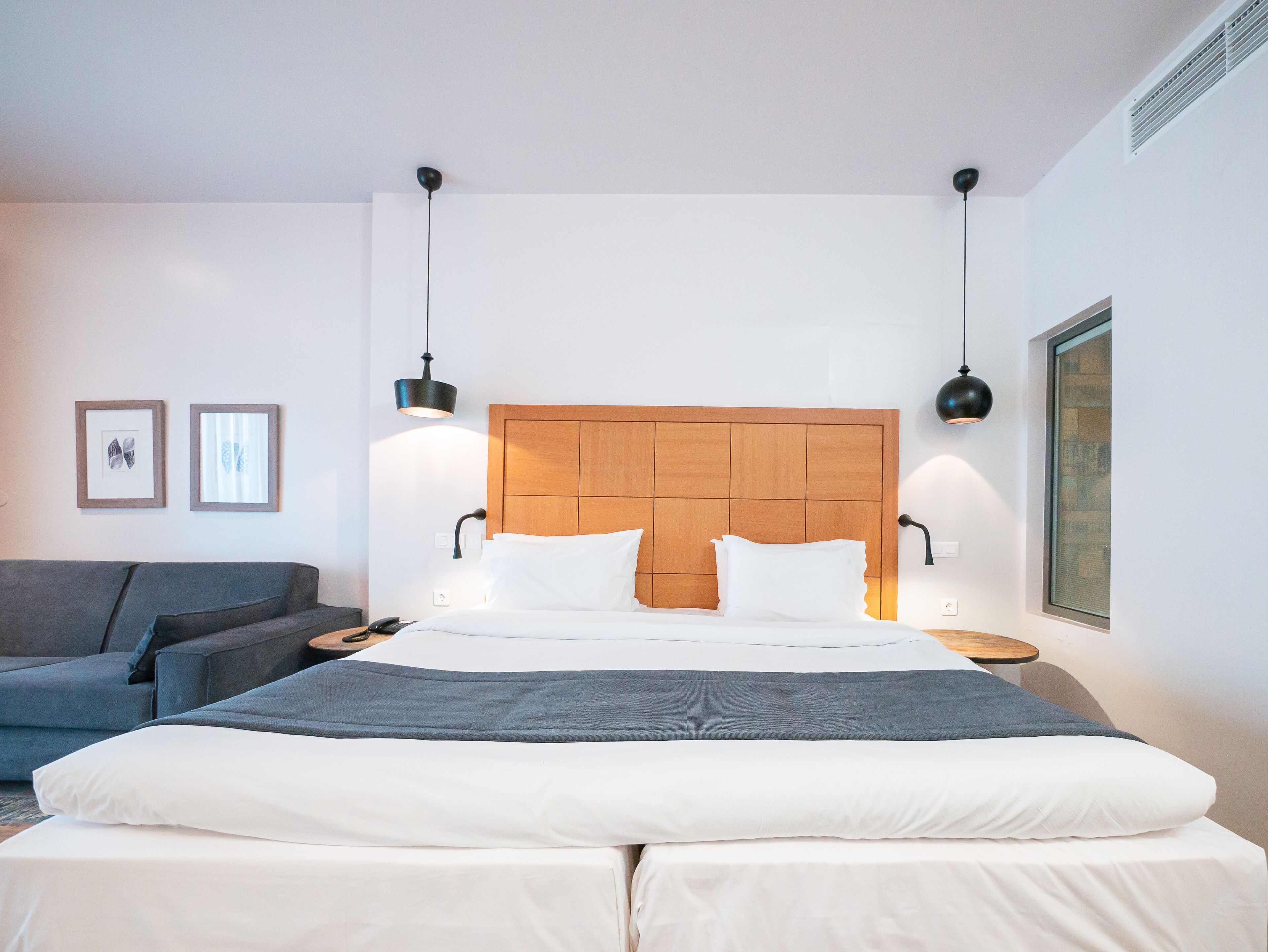 A modern bedroom with a wooden headboard, a grey sofa, and two bedside lamps.