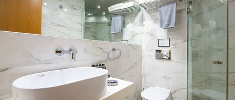A modern bathroom with a large white sink, a toilet, and a glass-enclosed shower area.