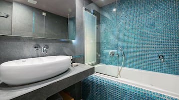 Un baño moderno con un lavamanos grande y blanco, una bañera con mosaicos azules y un espejo sobre el lavamanos.