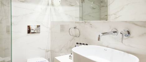 Un baño moderno con cabina de ducha de vidrio, inodoro blanco, una bañera grande independiente y pared de mármol.