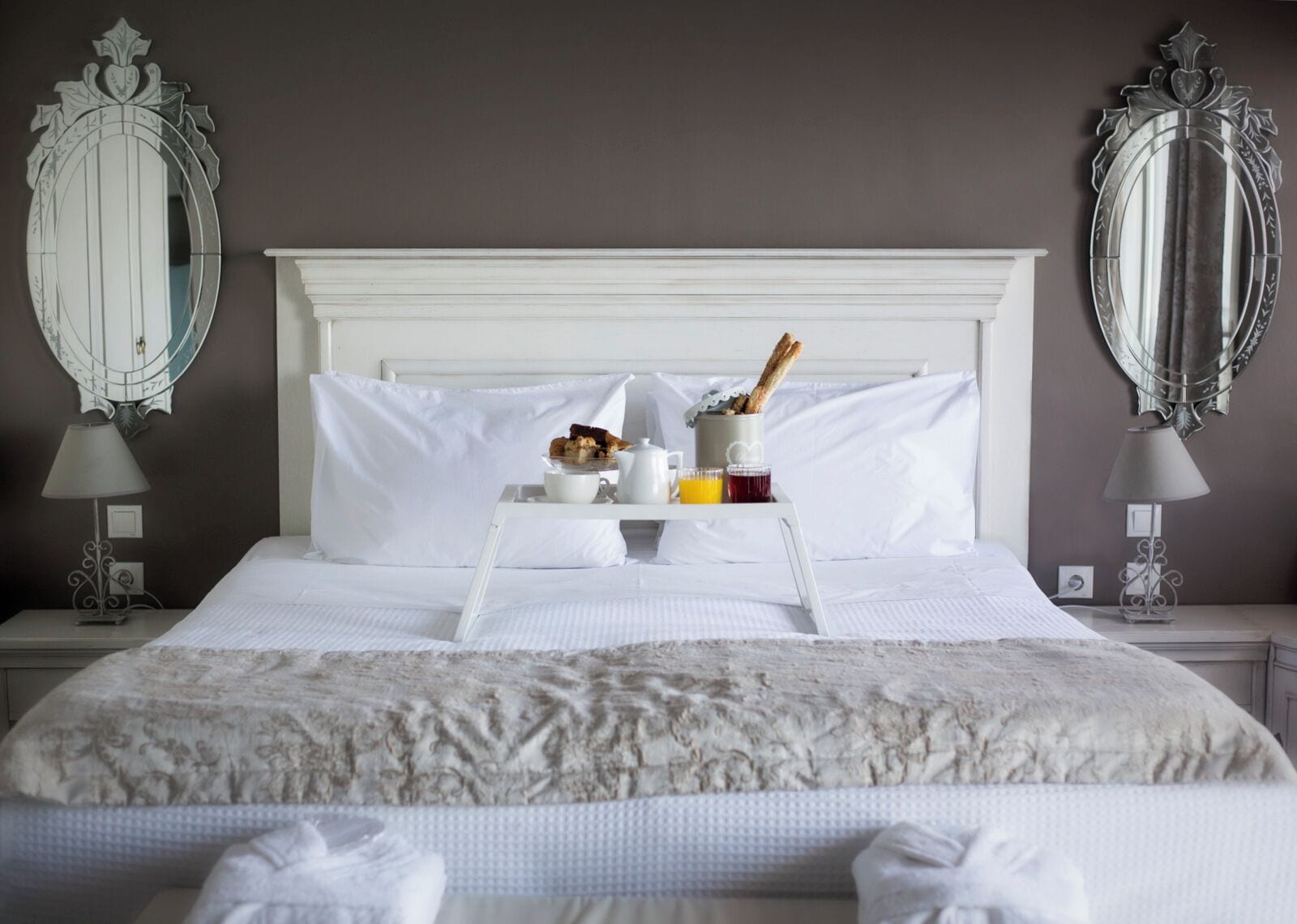 A neatly made bed with white linens, a tray with breakfast items, and two bedside tables with lamps.