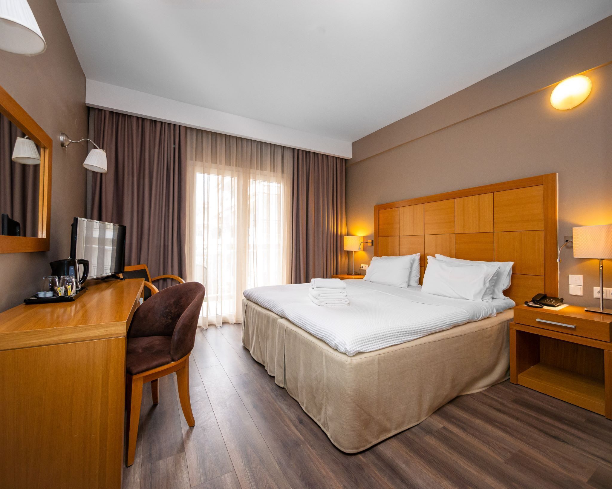 Habitación de hotel con cama, escritorio con cafetera, silla y mesita de noche con lámpara.