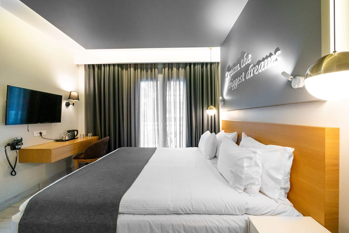 Habitación de hotel con cama, televisión, escritorio con lámpara y ventana con cortinas.