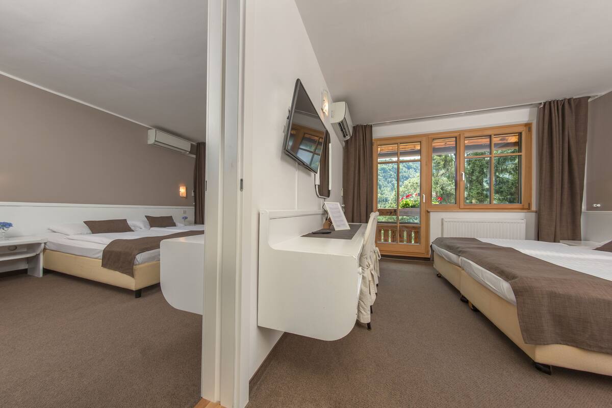 A hotel room with two beds, a desk, a TV, and a window with curtains.
