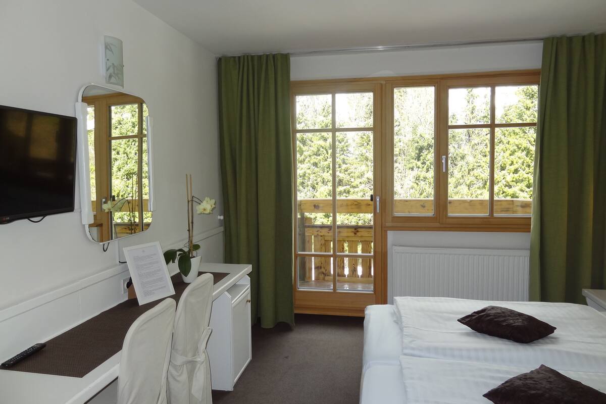 A hotel room with a bed, a desk with a chair, a television mounted on the wall, and a window with curtains.
