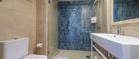 A bathroom with a toilet, a shower with blue tiles, and a sink with a towel rack.