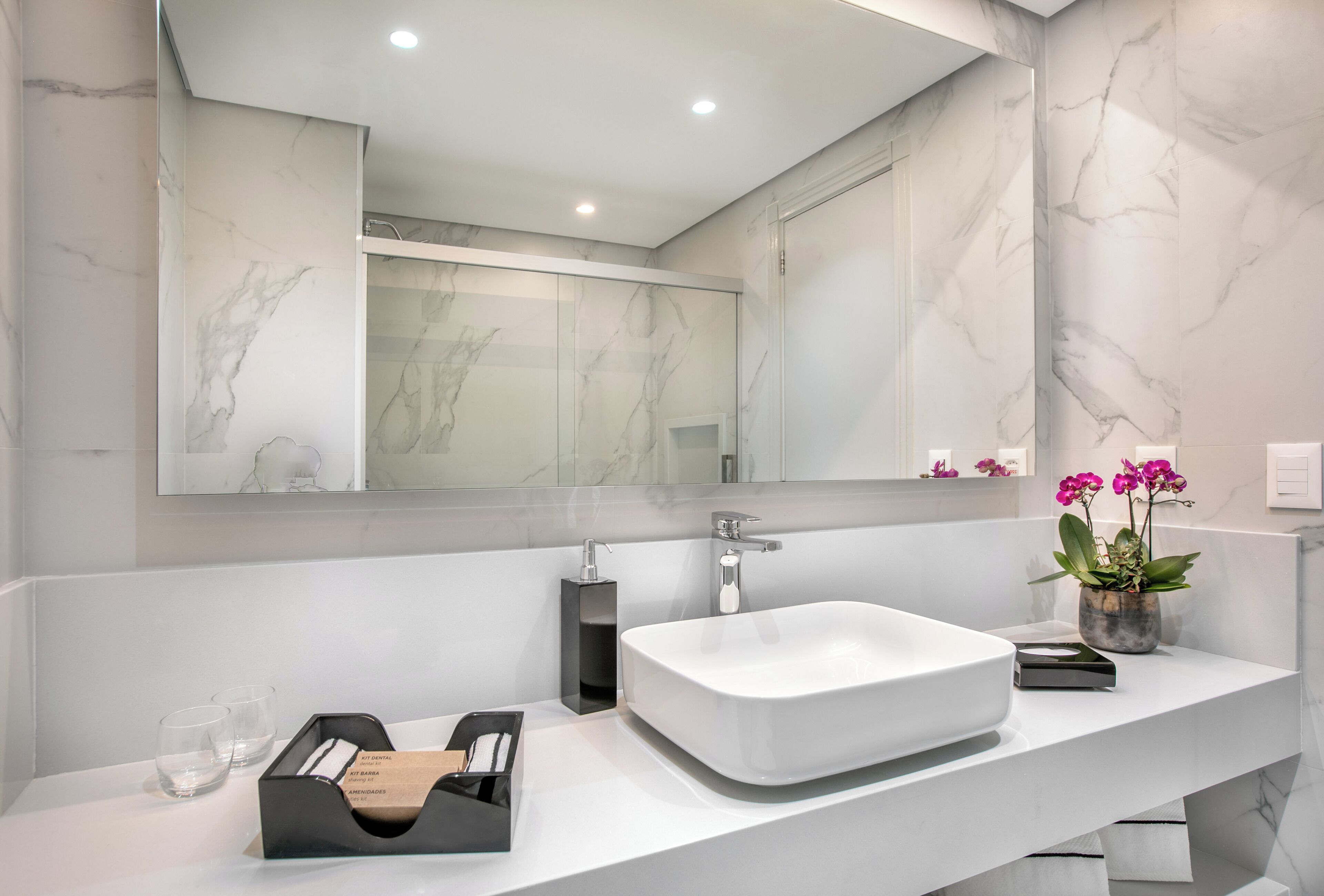 Un baño moderno con un espejo grande, un lavabo blanco y una pared de mármol.