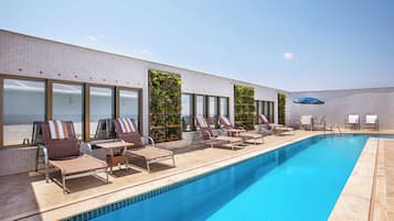 Un área junto a la piscina con sillones de descanso y una piscina azul.